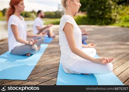 fitness, sport, yoga and healthy lifestyle concept - close up of people meditating in easy sitting pose on river or lake berth