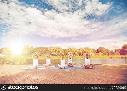 fitness, sport, yoga and healthy lifestyle concept - close up of people meditating in easy sitting pose on river or lake berth. close up of people making yoga exercises outdoors