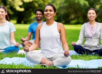 fitness, sport, yoga and healthy lifestyle concept - group of happy people meditating in lotus pose at summer park. group of happy people doing yoga at summer park