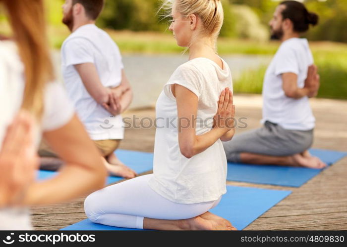 fitness, sport, yoga and healthy lifestyle concept - group of people exercising in reverse prayer pose on river or lake berth