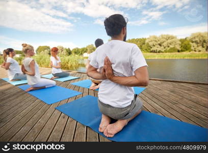 fitness, sport, yoga and healthy lifestyle concept - group of people exercising in reverse prayer pose on river or lake berth