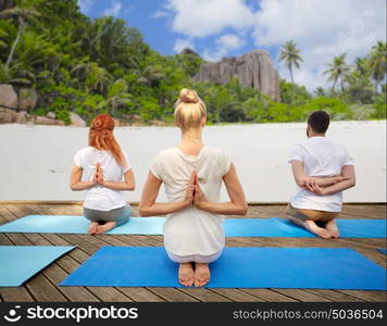 fitness, sport, yoga and healthy lifestyle concept - group of people exercising in reverse prayer pose over tropical beach background. group of people making yoga exercises over beach