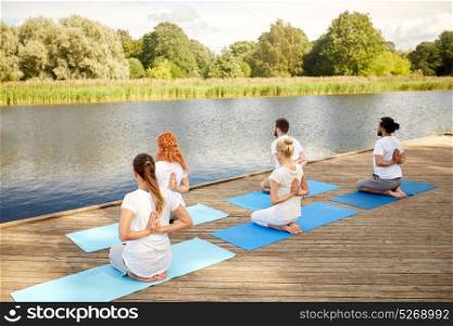 fitness, sport, yoga and healthy lifestyle concept - group of people exercising in reverse prayer pose on river or lake berth. group of people making yoga exercises outdoors