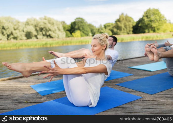 fitness, sport, yoga and healthy lifestyle concept - group of people making half-boat pose on mat outdoors on river or lake berth