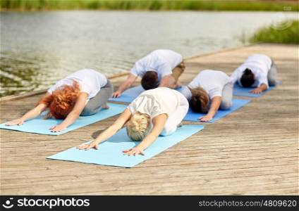 fitness, sport, yoga and healthy lifestyle concept - group of people making childs pose on river or lake berth