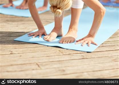 fitness, sport, yoga and healthy lifestyle concept - group of people making standing forward bend on mat outdoors