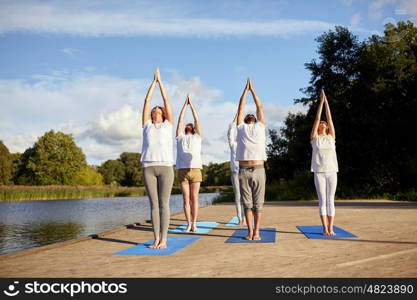 fitness, sport, yoga and healthy lifestyle concept - group of people making upward salute pose on river or lake berth