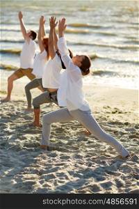 fitness, sport, yoga and healthy lifestyle concept - group of people making high lunge or crescent pose on beach