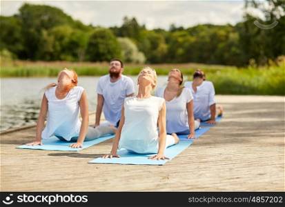 fitness, sport, yoga and healthy lifestyle concept - group of people making cobra pose on river or lake berth