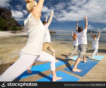 fitness, sport, yoga and healthy lifestyle concept - group of people making high lunge or crescent pose over exotic tropical beach background. group of people making yoga exercises outdoors