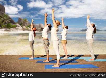 fitness, sport, yoga and healthy lifestyle concept - group of people making upward salute pose over tropical beach background. group of people making yoga exercises over beach