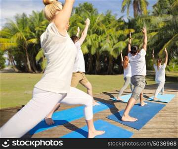 fitness, sport, yoga and healthy lifestyle concept - group of people making high lunge or crescent pose over natural background with palm trees . group of people making yoga exercises outdoors