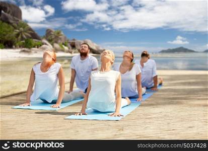 fitness, sport, yoga and healthy lifestyle concept - group of people making cobra pose over tropical beach background. group of people making yoga exercises over beach