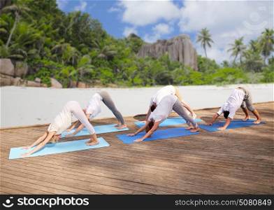 fitness, sport, yoga and healthy lifestyle concept - group of people making downward facing dog pose over tropical beach background. group of people making yoga dog pose over beach