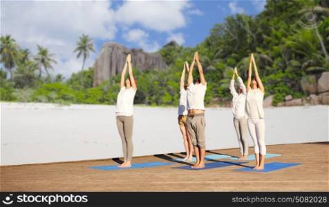 fitness, sport, yoga and healthy lifestyle concept - group of people making upward salute pose over tropical beach background. group of people making yoga exercises over beach