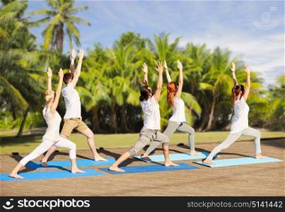 fitness, sport, yoga and healthy lifestyle concept - group of people making high lunge or crescent pose over exotic tropical background with palm trees. group of people making yoga exercises outdoors