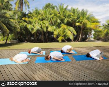 fitness, sport, yoga and healthy lifestyle concept - group of people making child pose over natural exotic background with palm trees. group of people making yoga exercises outdoors