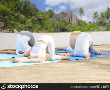 fitness, sport, yoga and healthy lifestyle concept - group of people making ear pressure pose over tropical beach background. group of people making yoga exercises over beach