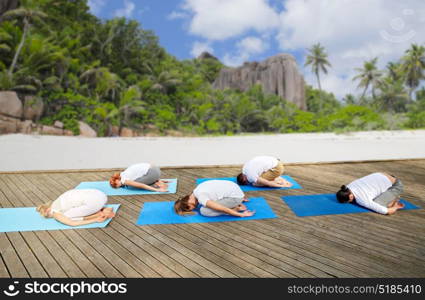 fitness, sport, yoga and healthy lifestyle concept - group of people making child pose over tropical beach background. group of people making yoga exercises over beach