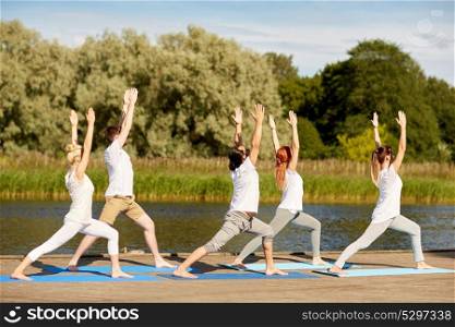 fitness, sport, yoga and healthy lifestyle concept - group of people making high lunge or crescent pose on river berth. group of people making yoga exercises outdoors