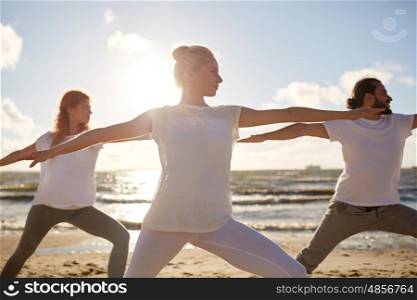 fitness, sport, yoga and healthy lifestyle concept - group of people making warrior pose on beach