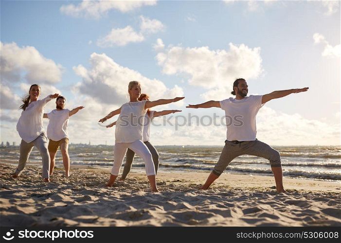 fitness, sport, yoga and healthy lifestyle concept - group of people making warrior pose on beach. group of people making yoga exercises on beach