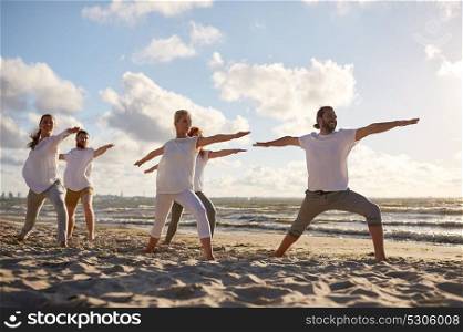 fitness, sport, yoga and healthy lifestyle concept - group of people making warrior pose on beach. group of people making yoga exercises on beach