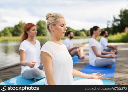 fitness, sport, yoga and healthy lifestyle concept - group of people meditating in lotus pose on river or lake berth