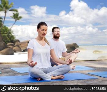 fitness, sport, yoga and healthy lifestyle concept - group of people meditating in lotus pose over exotic tropical beach background. people meditating in yoga lotus pose outdoors