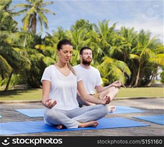 fitness, sport, yoga and healthy lifestyle concept - group of people meditating in lotus pose over exotic natural background with palm trees. people meditating in yoga lotus pose outdoors