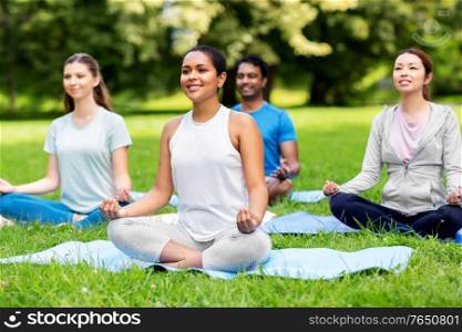 fitness, sport, yoga and healthy lifestyle concept - group of people meditating in lotus pose at summer park. group of people doing yoga at summer park