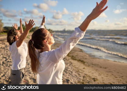 fitness, sport, yoga and healthy lifestyle concept - group of people meditating on beach