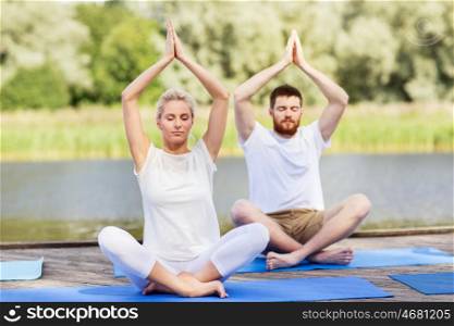 fitness, sport, yoga and healthy lifestyle concept - people meditating in lotus pose on river or lake berth