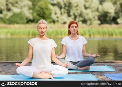 fitness, sport, yoga and healthy lifestyle concept - women meditating in lotus pose on river or lake berth