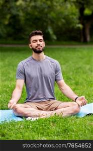 fitness, sport, yoga and healthy lifestyle concept - young man meditating in lotus pose at summer park. young man meditating at summer park