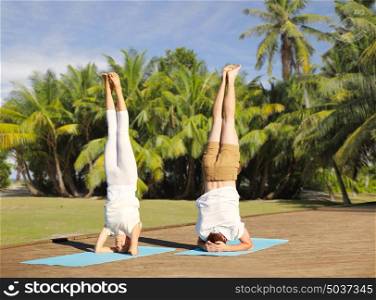 fitness, sport, yoga and people concept - couple making headstand pose on mat over natural background with palm trees . couple making yoga headstand on mat outdoors