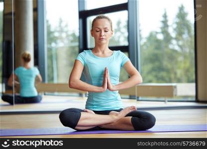 fitness, sport, yoga and people concept - happy woman with closed eyes meditating in lotus pose on mat in gym