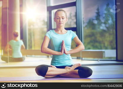 fitness, sport, yoga and people concept - happy woman with closed eyes meditating in lotus pose on mat in gym. happy woman meditating in lotus pose on mat