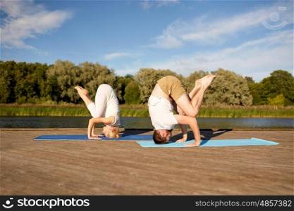 fitness, sport, yoga, people and healthy lifestyle concept - couple making headstand outdoors on river or lake berth