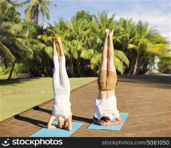 fitness, sport, yoga, people and healthy lifestyle concept - couple making headstand pose on mat over natural exotic background with palm trees. couple making yoga headstand on mat outdoors