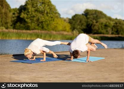 fitness, sport, yoga, people and healthy lifestyle concept - couple making side crane pose on mat on river or lake berth