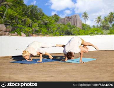 fitness, sport, yoga, people and healthy lifestyle concept - couple making side crane pose on mat over tropical beach background. couple making yoga side crane pose over beach