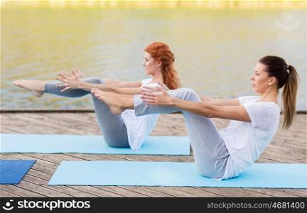fitness, sport, yoga, people and healthy lifestyle concept - women making half-boat pose on mat outdoors on river or lake berth