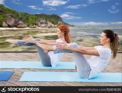 fitness, sport, yoga, people and healthy lifestyle concept - women making half-boat pose on mat outdoors over exotic tropical beach background. women making yoga in half-boat pose outdoors