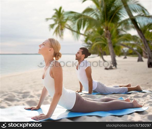 fitness, sport, yoga, people and lifestyle concept - happy couple making yoga exercises on tropical beach