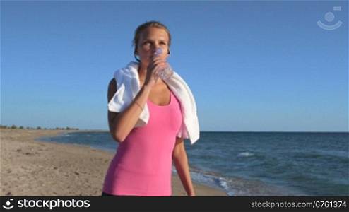 Fitness sporty girl exercising on beach taking break to drink water medium shot