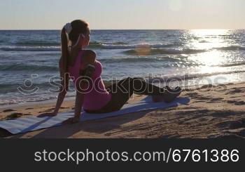 Fitness sporty woman relaxing after workout while listening music on beach at sunset