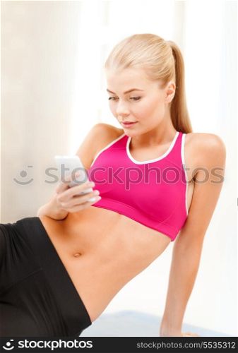 fitness, technology and exercise concept - smiling woman sitting on the floor and looking into smartphone