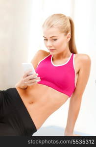 fitness, technology and exercise concept - smiling woman sitting on the floor and looking into smartphone