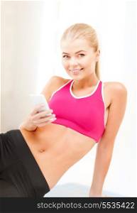 fitness, technology and exercise concept - smiling woman sitting on the floor and looking into smartphone